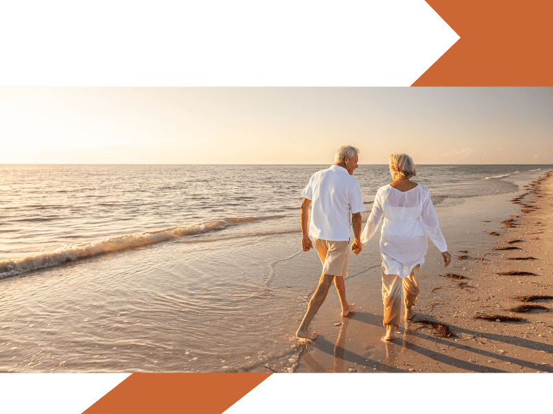 Retired couple holding hands walking along a deserted beach and sunset.