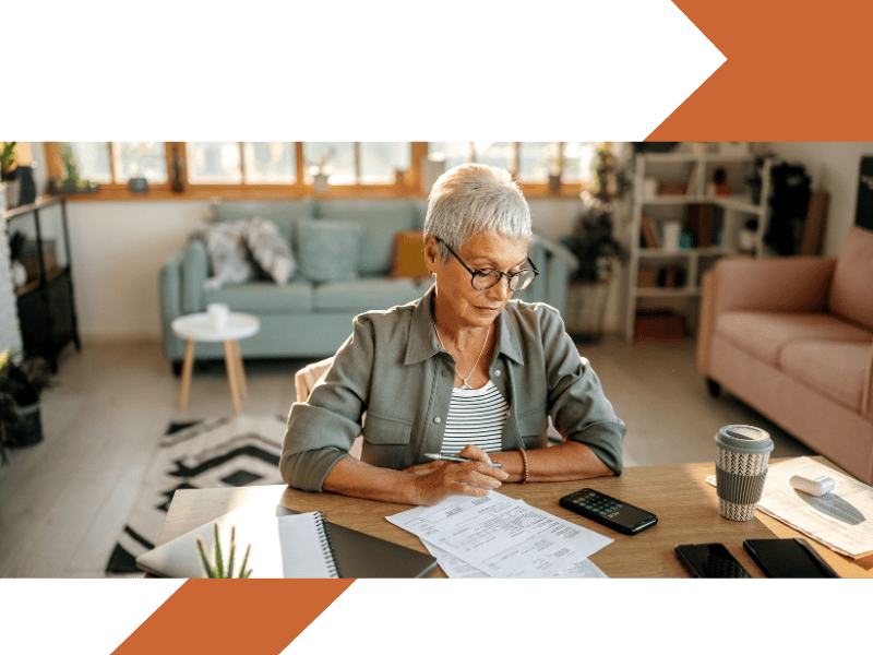 Clients we advise A middle-aged lady at her desk looking to sign documents with a pen in her hand and a coffee on the desk in a takeaway cup.
