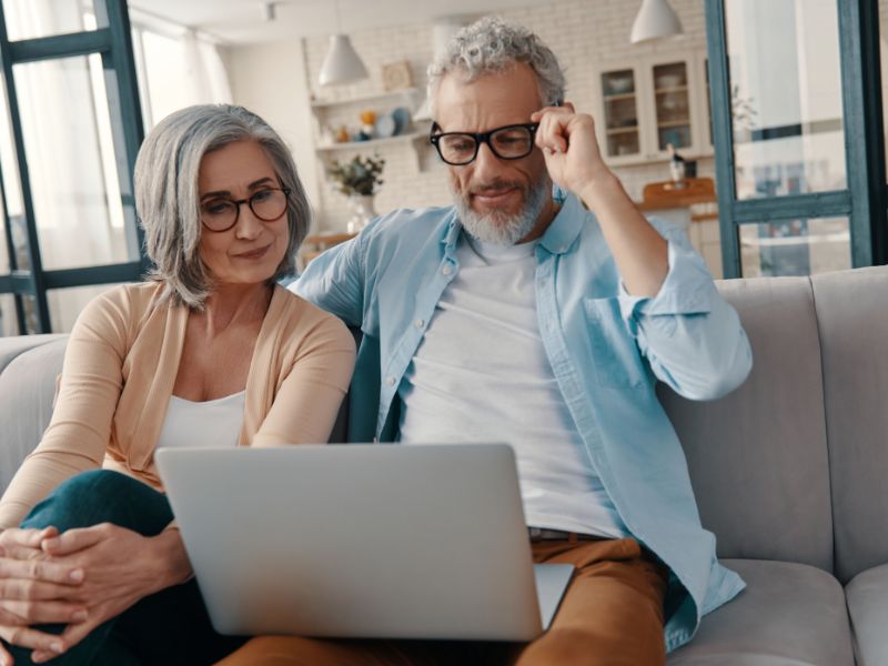 A retirement aged couple sitting on the sofa looking at laptop.